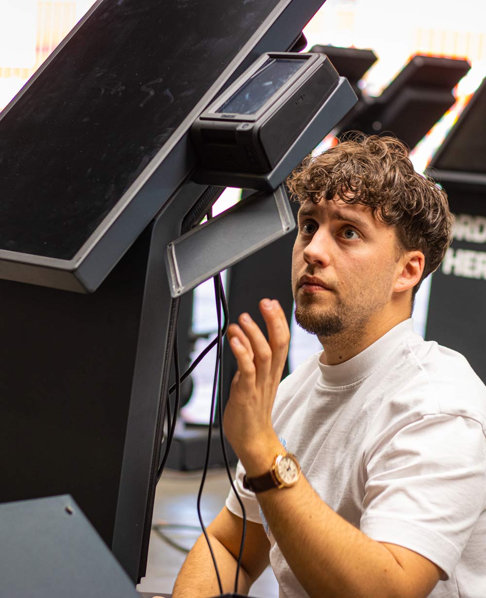 Man with curly hair (Bastiaan Onesix) and a beard intently interacting with a touchscreen device.